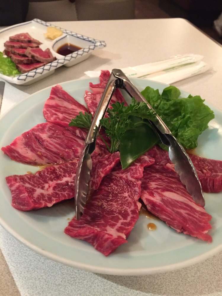 Marbled prime short rib arranged on a plate with tongs and parsley, beef tataki in background